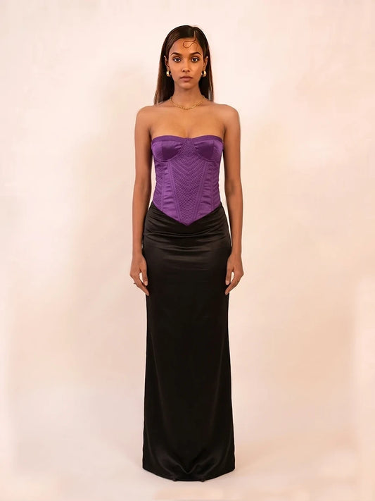 Model wearing Vana, a deep purple structured silk corset with detailed topstitching and a sculpted bodice, paired with a black draped skirt.